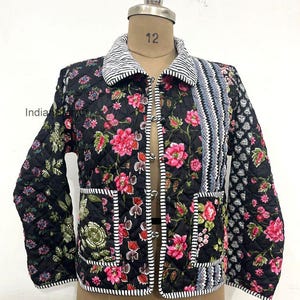 May include: Black quilted jacket with a floral pattern in pink and green. The jacket features a striped collar and trim, with a mix of floral and geometric patterns on the sleeves and pockets. The jacket is displayed on a mannequin.
