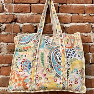 Peut inclure: Un grand sac fourre-tout coloré avec un motif paisley. Le sac a un fond crème avec des accents bleus, verts, orange et roses. Le sac a deux longues lanières et une large ouverture.
