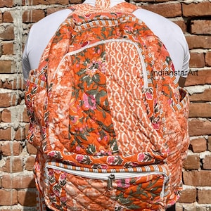 Może przedstawiać: Duży pomarańczowy i biały pikowany plecak z kwiatowymi wzorami. Plecak ma kieszeń zapinaną na zamek błyskawiczny z przodu i biały suwak.