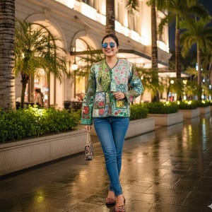 Può includere: Giacca patchwork colorata con un design floreale, abbinata a jeans blu. La giacca ha uno scollo a V e maniche lunghe. Una piccola borsa fantasia e occhiali da sole completano il look. Lo sfondo mostra una strada cittadina con palme.