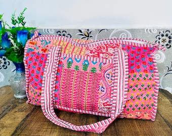 May include: A pink and white patchwork tote bag with a floral print. The bag has two long straps and a zipper closure.