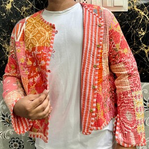 Könnte beinhalten: Eine rote und orangefarbene Patchwork-Steppjacke mit Knopfleiste. Die Jacke hat ein gestreiftes Muster auf der Vorderseite und florale Muster auf den Ärmeln.