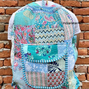 May include: A patchwork style backpack made of quilted fabric in shades of blue, green, and pink. The backpack has a large pocket on the front and a smaller pocket on the top.