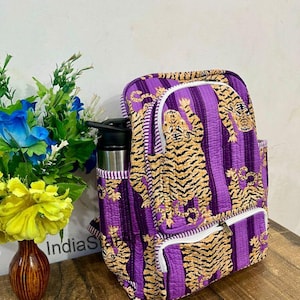 May include: A quilted backpack with a purple and white striped pattern, featuring tiger illustrations in shades of tan and black. The backpack has white zippers and a side pocket. A water bottle is in the side pocket.