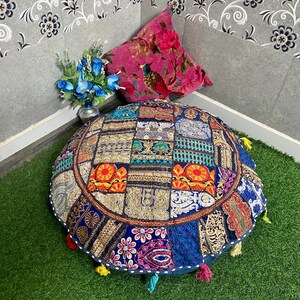 Puede incluir: Un cojín de suelo redondo y multicolor con un diseño de patchwork. El cojín está hecho de varias telas y tiene detalles bordados. Tiene borlas y flecos alrededor de los bordes.