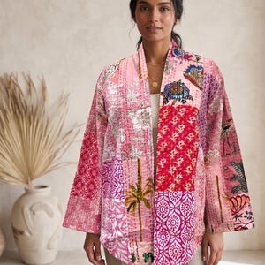 May include: A long-sleeved open-front jacket featuring a patchwork design of various pink, red, and white floral and botanical patterns. The garment is constructed with visible running stitch quilting details throughout the fabric panels.
