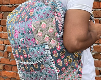 Peut inclure: Un sac à dos gris en patchwork avec des motifs floraux et des bordures blanches. Le sac à dos a une grande poche sur le devant et des bretelles réglables.