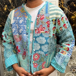May include: A blue and white quilted jacket with a floral and cartoon print. The jacket has a button closure and long sleeves.