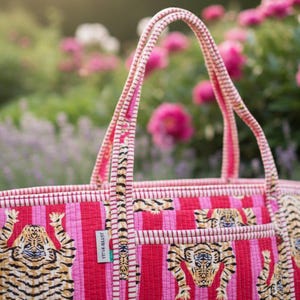 May include: A quilted tote bag with a vibrant pink and red striped pattern. The bag features tiger illustrations and a matching striped handle. A small tag reads "YETI & BEAST".