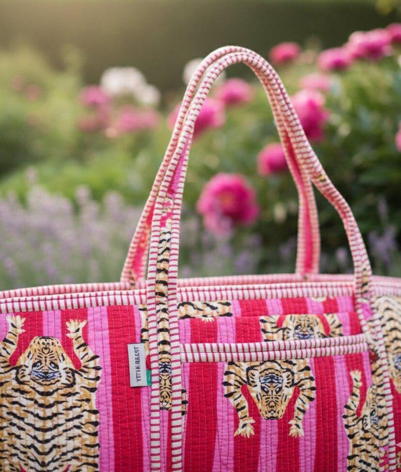 May include: A quilted tote bag with a vibrant pink and red striped pattern. The bag features tiger illustrations and a matching striped handle. A small tag reads "YETI & BEAST".
