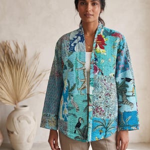 Puede incluir: Una chaqueta acolchada con un diseño de patchwork en tonos turquesa, azul y blanco. La tela muestra varios patrones estampados que incluyen aves tropicales, tigres y motivos florales, con detalles de costuras visibles.