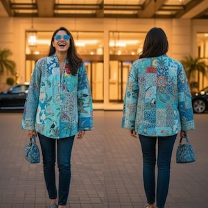 May include: A blue patchwork jacket with floral and bird motifs, worn with dark blue jeans. The jacket has a relaxed fit and wide sleeves. The person is carrying a matching blue handbag. The jacket's design incorporates various shades of blue and white. A unique piece of apparel.