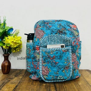 May include: A quilted backpack with a vibrant floral pattern in shades of blue, red, and pink. The backpack features multiple pockets, including a side pocket for a water bottle. The interior has a striped lining, and the exterior has a quilted design.