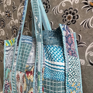 May include: A large, patchwork tote bag made from recycled fabric. The bag is blue, green, and white with a variety of patterns. The bag has two long straps and is perfect for carrying groceries or other items.