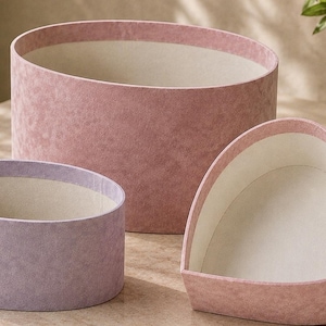 May include: A set of three decorative storage boxes with a textured finish. One large round pink box, one smaller oval lavender box, and one heart-shaped pink box. Each container features a smooth, off-white interior lining.