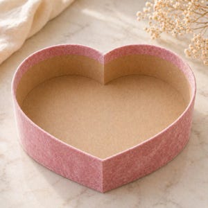 May include: A heart-shaped box with a soft, pink exterior and a light brown interior. The box is empty and has a simple, elegant design. The box is likely used for gifts or storage.