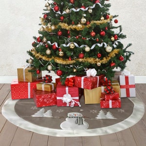 May include: A round, taupe-coloured Christmas tree skirt featuring a central white snowman appliqu&eacute; wearing a black and white chequered scarf, surrounded by white embroidered pine trees and snowflakes, finished with a wide, solid white border trim.