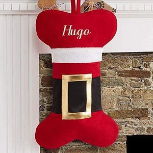 May include: A red and white personalised Christmas stocking shaped like a bone with the name "Hugo" embroidered on it.