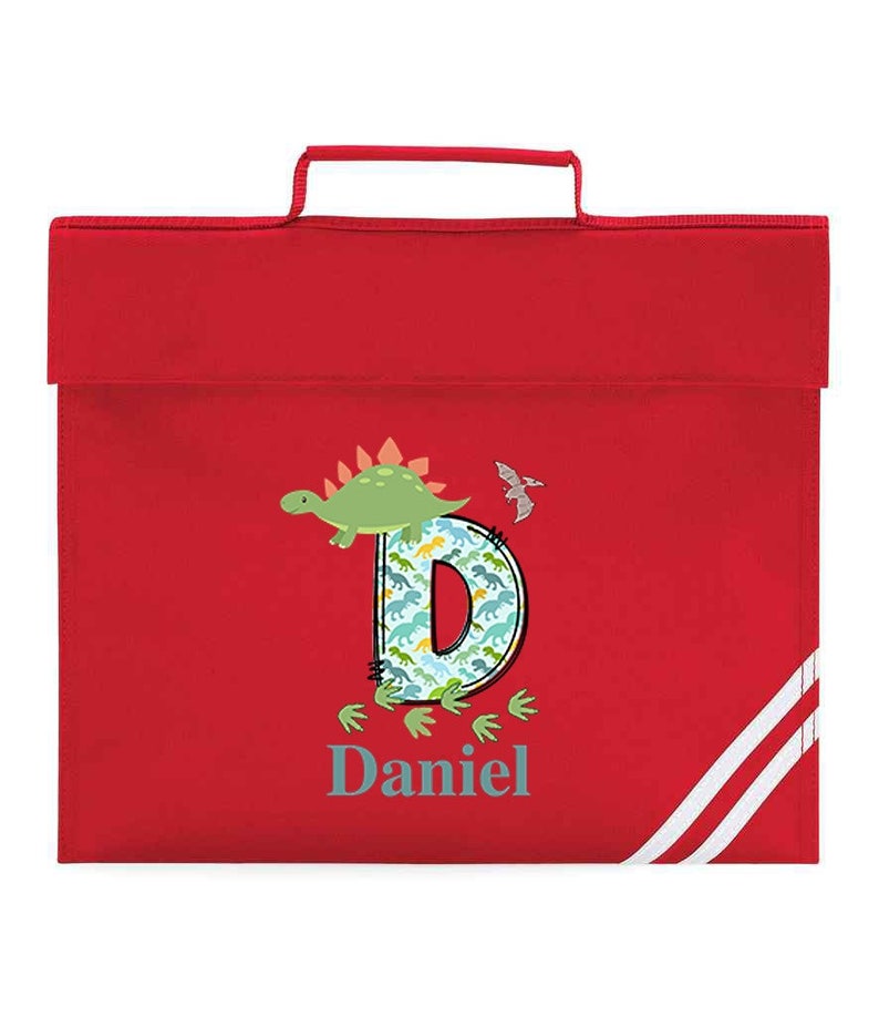 May include: Red book bag with white stripes. The bag features a dinosaur design with the letter D and the name Daniel.