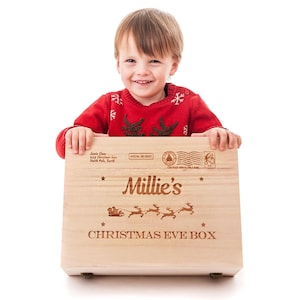 Puede incluir: Una caja de madera personalizada para la Nochebuena con el nombre "Millie's" grabado en la parte delantera. La caja presenta un trineo de Pap&aacute; Noel con renos y el texto "Christmas Eve Box".