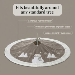 May include: A circular taupe Christmas tree skirt with a white faux fur border, featuring an embroidered snowman wearing a plaid scarf, white pine trees, and snowflakes. The text reads: Fits beautifully around any standard tree, Generous 78cm diameter, Hides unsightly metal or plastic bases, Drapes elegantly over cables.