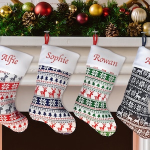 May include: Four personalised Christmas stockings with a Scandinavian-inspired design. The stockings are red, blue, green and black with white accents. The stockings are hung on a white mantelpiece with a green garland and red and gold baubles.