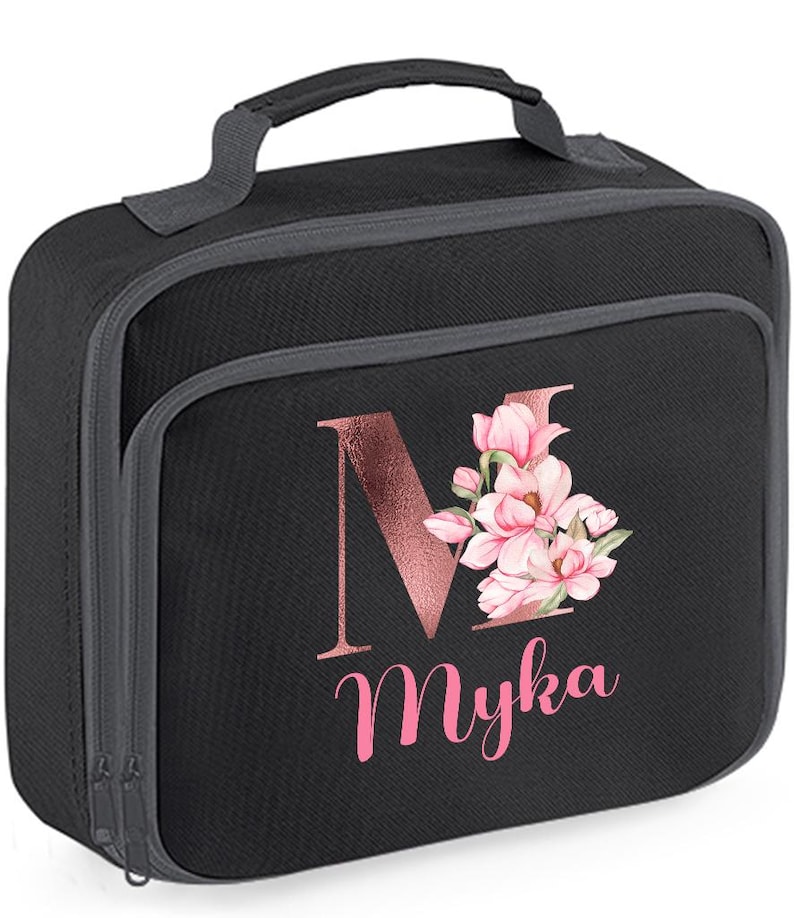 Puede incluir: Bolsa de almuerzo negra con asa y ribete grises. La parte delantera presenta la letra "M" en oro rosa con detalles florales rosas y el nombre "Myka" en escritura rosa. La bolsa tiene cierre de cremallera.