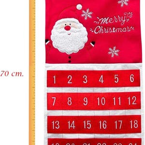 May include: Red and white Christmas advent calendar, 70 cm tall and 50 cm wide, with Santa Claus design and the words "merry Christmas". It has 24 numbered pockets for each day of December leading up to Christmas. The name "Daniel" is written at the top.