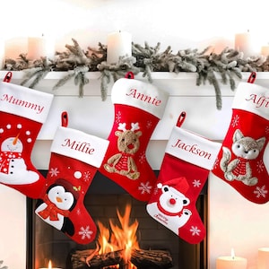 May include: Five red and white Christmas stockings with different embroidered designs and names: Mummy, Millie, Annie, Jackson, and Alfie.