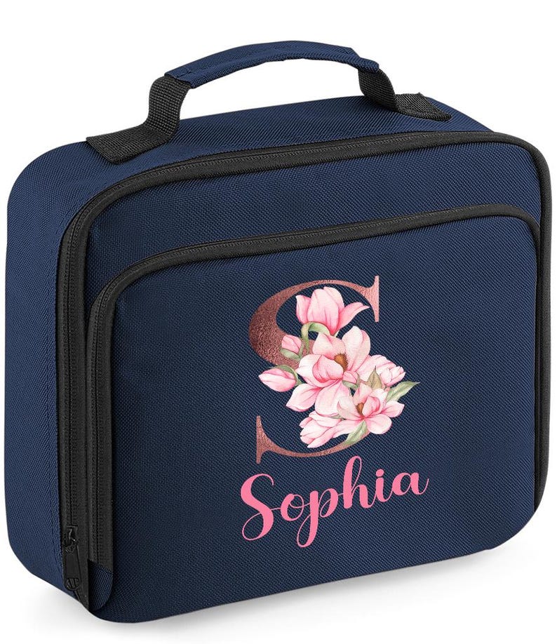 Puede incluir: Bolsa de almuerzo azul marino con asa y cremallera negras. La parte delantera presenta un dise&ntilde;o floral con la letra "S" y el nombre "Sophia" en rosa. Dise&ntilde;ada para transportar alimentos y bebidas.