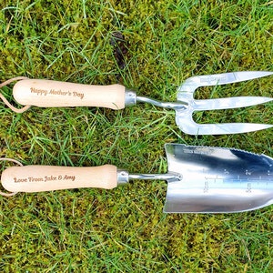May include: A set of two gardening tools with wooden handles. The tools are engraved with the text "Happy Mother's Day" and "Love From Jake & Amy".