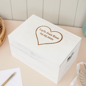 May include: White wooden keepsake box with a heart-shaped cutout and engraved inscription "Layla Joan Ruse 24.05.2021".