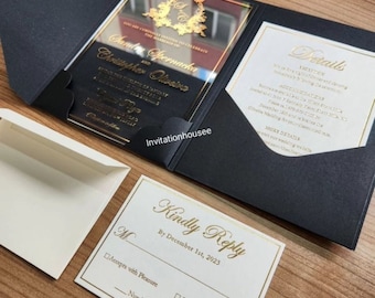 Könnte beinhalten: Schwarze und goldene Hochzeitseinladung mit einem transparenten Acryldeckel. Die Einladung zeigt ein goldenes Blumenmuster und den Text "You are cordially invited to celebrate the marriage of Samantha Spernacka and Christopher Oliveira". Die Einladung enthält auch eine RSVP-Karte mit dem Text "Kindly Reply by December 1st, 2023".