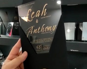 Könnte beinhalten: Schwarze und goldene Hochzeitseinladung mit einer transparenten Acrylabdeckung. Die Einladung trägt die Namen "Leah & Anthony" und das Datum "08. August 2021".