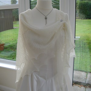 May include: A white lace shawl draped over a white dress form. The shawl has a delicate, intricate pattern and is made of a soft, lightweight fabric.