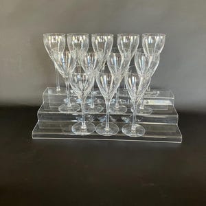 May include: A collection of clear crystal wine glasses with a tall, slender design. The glasses are arranged on a tiered, transparent display, showcasing their intricate, etched patterns. The stemware is ideal for formal dining or special occasions.