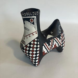 May include: A black ceramic vessel shaped like a stylized animal with a tall neck and four legs. The surface is decorated with white and terracotta geometric patterns, including checkerboard squares, zigzags, and fine line drawings.