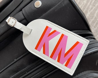 May include: White luggage tag with the initials "KM" in pink and orange letters.