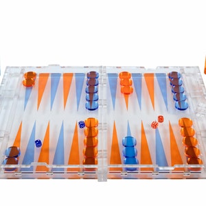 May include: A clear plastic backgammon set with orange and blue playing pieces and dice. The board is open and ready for play.