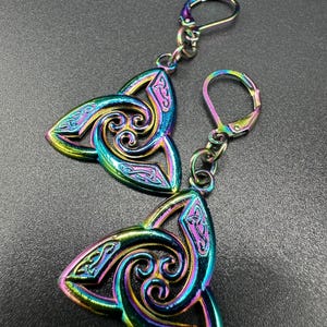 May include: A pair of iridescent Celtic knot earrings. Each earring features a three-pointed design with intricate swirling patterns and a lever-back closure. The earrings display a vibrant spectrum of colors, including blues, greens, and purples.