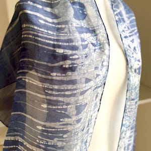 Può includere: Una sciarpa di seta blu e bianca con un motivo batik. La sciarpa è drappeggiata su un manichino.