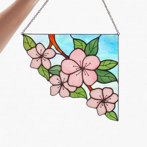 May include: A stained glass window hanging with a chain. The window is shaped like a triangle and features a design of pink flowers with green leaves on a blue background.