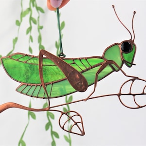 May include: A stained glass grasshopper ornament with green wings and copper wire details, perched on a copper wire branch with leaves.