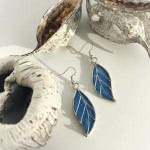 Op de afbeelding: Een paar blauwe glas-in-lood bladeren oorbellen met zilveren draad accenten. De oorbellen hangen aan zilveren haken.
