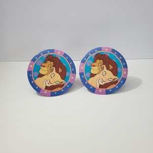 Puede incluir: Dos platos de papel redondos azules y rosas con una imagen de Simba y Nala de la película El Rey León. Los platos tienen un patrón de estrellas blancas alrededor del borde.