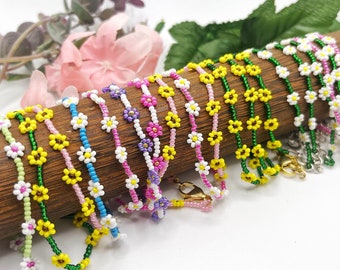 Puede incluir: Una colección de pulseras de cuentas coloridas con diseños de margaritas. Las pulseras están hechas con cuentas pequeñas y coloridas y presentan una variedad de colores, incluyendo verde, amarillo, rosa, azul y morado.