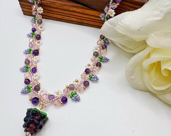 May include: A beaded necklace featuring a dark purple blackberry-shaped pendant, accented with small white flower beads, light pink crystal beads, and round purple amethyst-colored stones, all strung together on a delicate gold-toned chain.