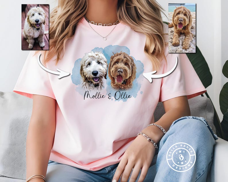 May include: A light pink short-sleeved t-shirt featuring a graphic print of two dogs with the names Mollie & Ollie written below them. The design includes a blue watercolor-style background and two smaller inset photos of the dogs above.
