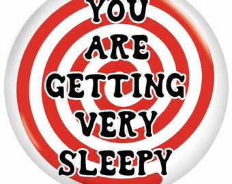 Puede incluir: Un botón circular con un patrón de espiral rojo y blanco. El texto "YOU ARE GETTING VERY SLEEPY" está impreso en letras mayúsculas negras y negritas en el centro del diseño en espiral, creando un efecto visual hipnótico.