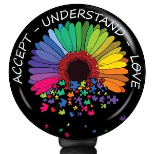 May include: A round, black button with a colorful sunflower design. The sunflower petals are rainbow-colored, and the center is a dark red. The words "ACCEPT - UNDERSTAND - LOVE" are written around the edge.
